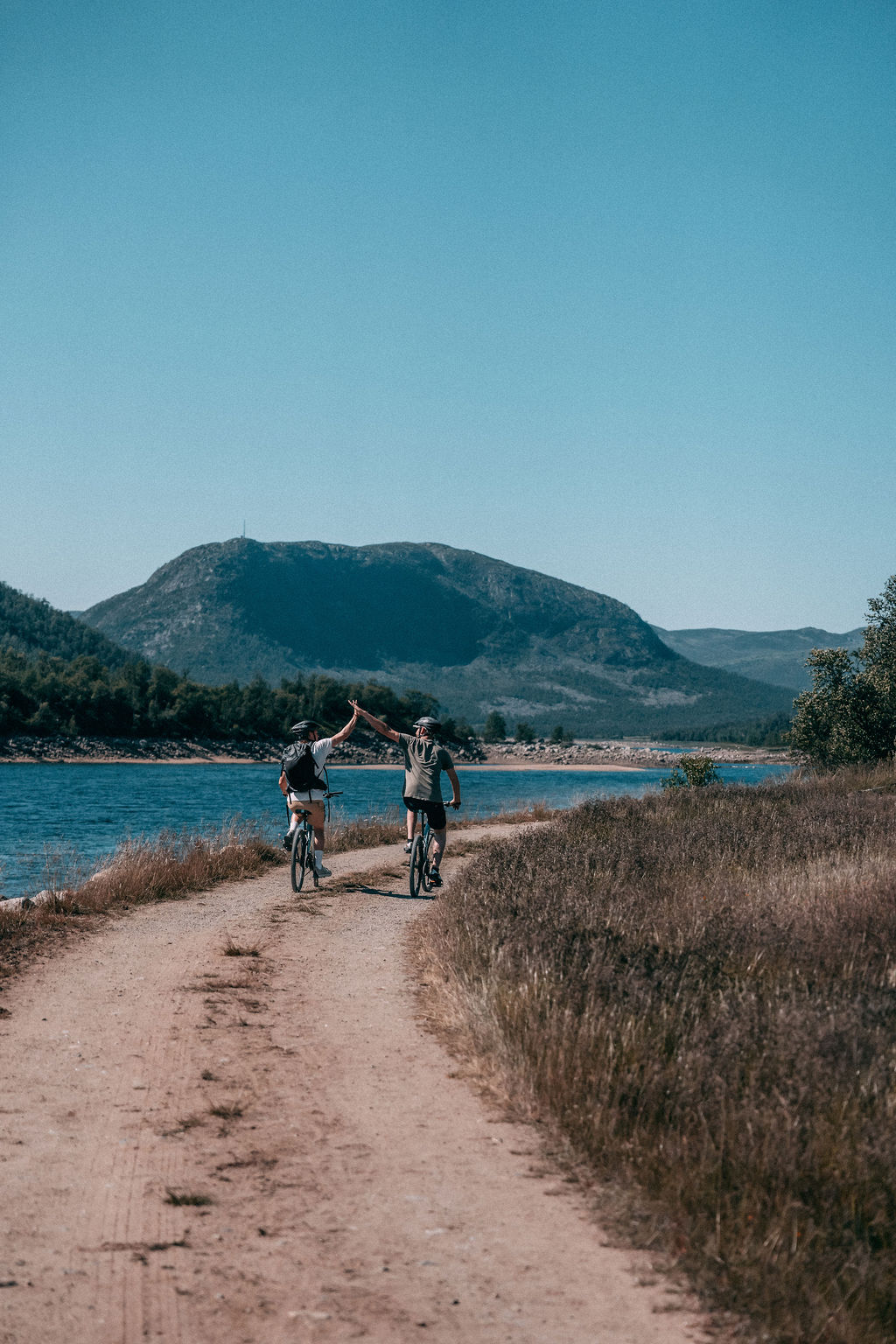 To syklister på grusvei langs blått fjellvann i Rauland